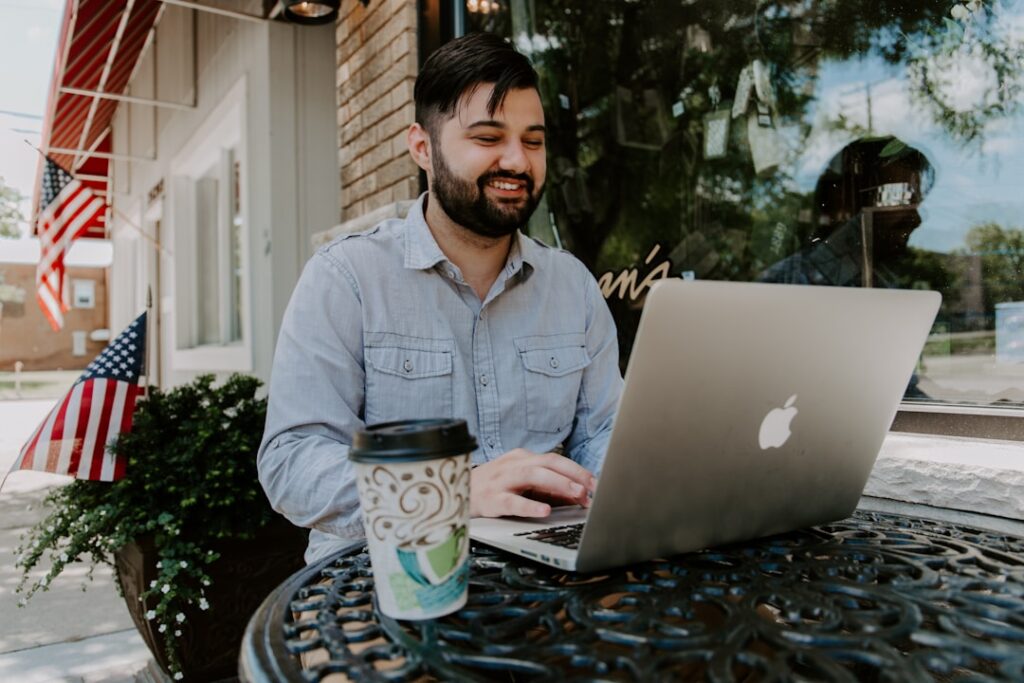 The Benefits of Using Faxing Software for Small Businesses A man sitting outdoors at a coffee shop, working on his laptop using faxing software to enhance cost-effectiveness for his small business